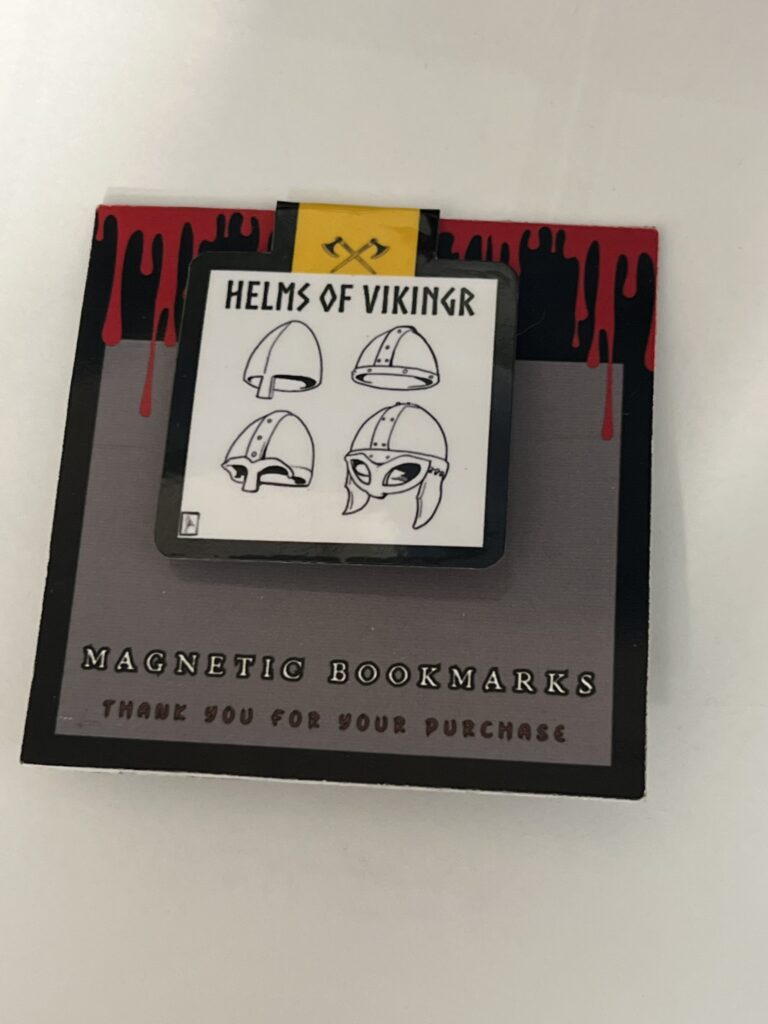 Magnetic bookmark titled "Helms of Vikingr" featuring four distinct Viking helmet designs. Mounted on a custom backing card with a red dripping paint motif.