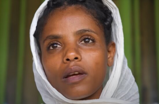 This image features Muluwork, the Ethiopian woman known for her extraordinary claim of living without food or water for 16 years. She is shown wearing a white headscarf, with a calm and contemplative expression, set against a green background that emphasizes her serene presence.