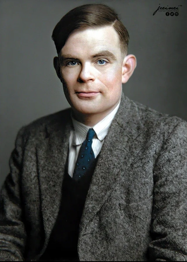 A colorized portrait of Alan Turing in his later years, dressed in a tweed jacket, white shirt, and blue tie. He faces forward with a slight smile, his eyes reflecting a thoughtful demeanor. 