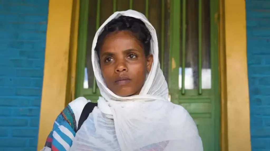 This image features Muluwork, the Ethiopian woman known for her extraordinary claim of living without food or water for 16 years. She is shown wearing a white headscarf, with a calm and contemplative expression, set against a green background that emphasizes her serene presence.