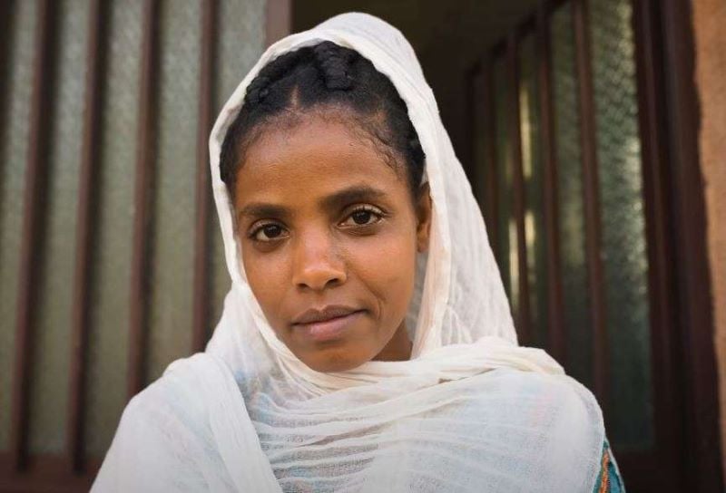 This image features Muluwork, the Ethiopian woman known for her extraordinary claim of living without food or water for 16 years. She is shown wearing a white headscarf, with a calm and contemplative expression.