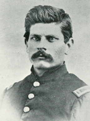 A historic black and white photograph of a young Ambrose Bierce in military uniform during the American Civil War. He has a serious expression and a thick mustache, and his coat has brass buttons.