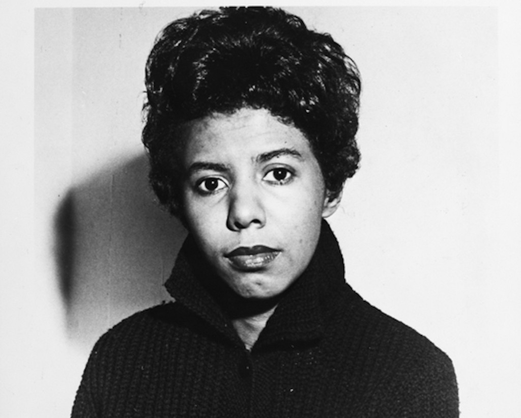 Black-and-white portrait of Lorraine Hansberry wearing a dark sweater, looking directly at the camera with a serious expression. The background is plain.