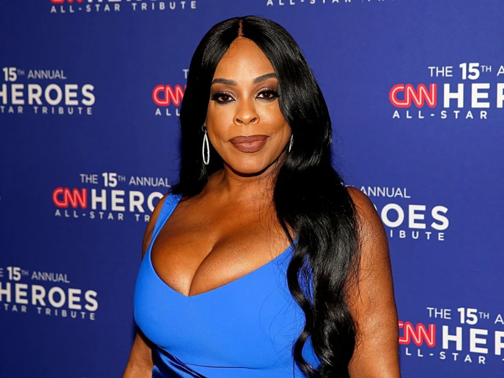 Niecy Nash-Betts in a bold blue dress posing on the red carpet at the 15th Annual CNN Heroes All-Star Tribute, with long black hair styled in soft waves and silver hoop earrings.