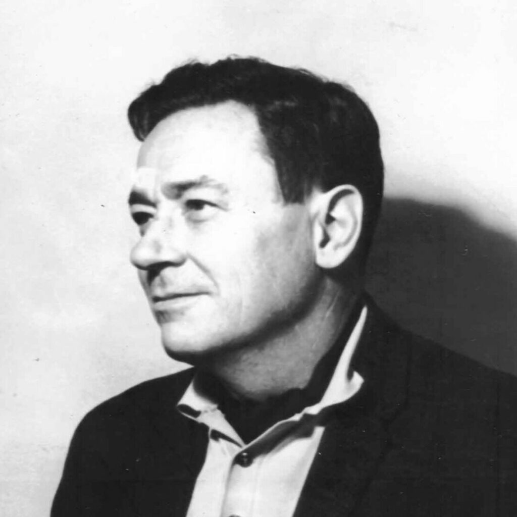 Black-and-white portrait of a younger Michael Bronski with short dark hair in a suit jacket and open-collar shirt, looking to the left with a contemplative expression.