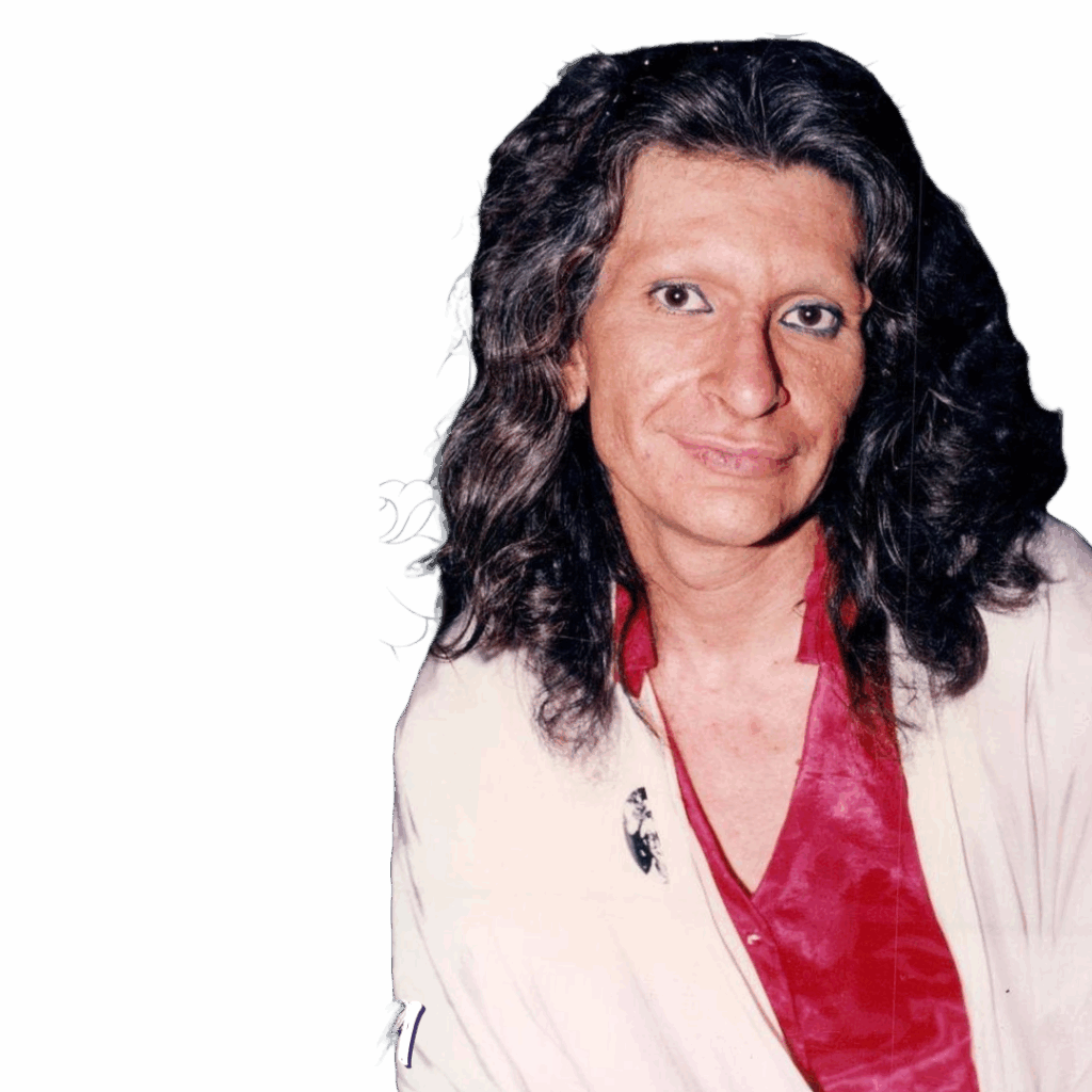 A color photograph of Sylvia Rivera in her later years, smiling with soft eye makeup, long curly hair, and wearing a red shirt with a white overcoat. A pin featuring Marsha P. Johnson is visible on her lapel.