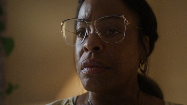 Close-up of Niecy Nash-Betts wearing oversized clear-framed glasses and hoop earrings, portraying Glenda Cleveland in a somber moment from Dahmer – Monster: The Jeffrey Dahmer Story.