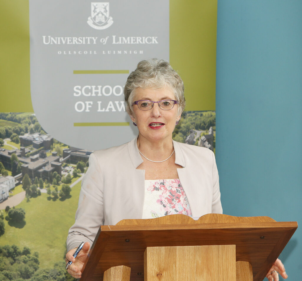 Katherine Zappone speaking at a podium at the University of Limerick School of Law, wearing a light blazer and floral blouse.