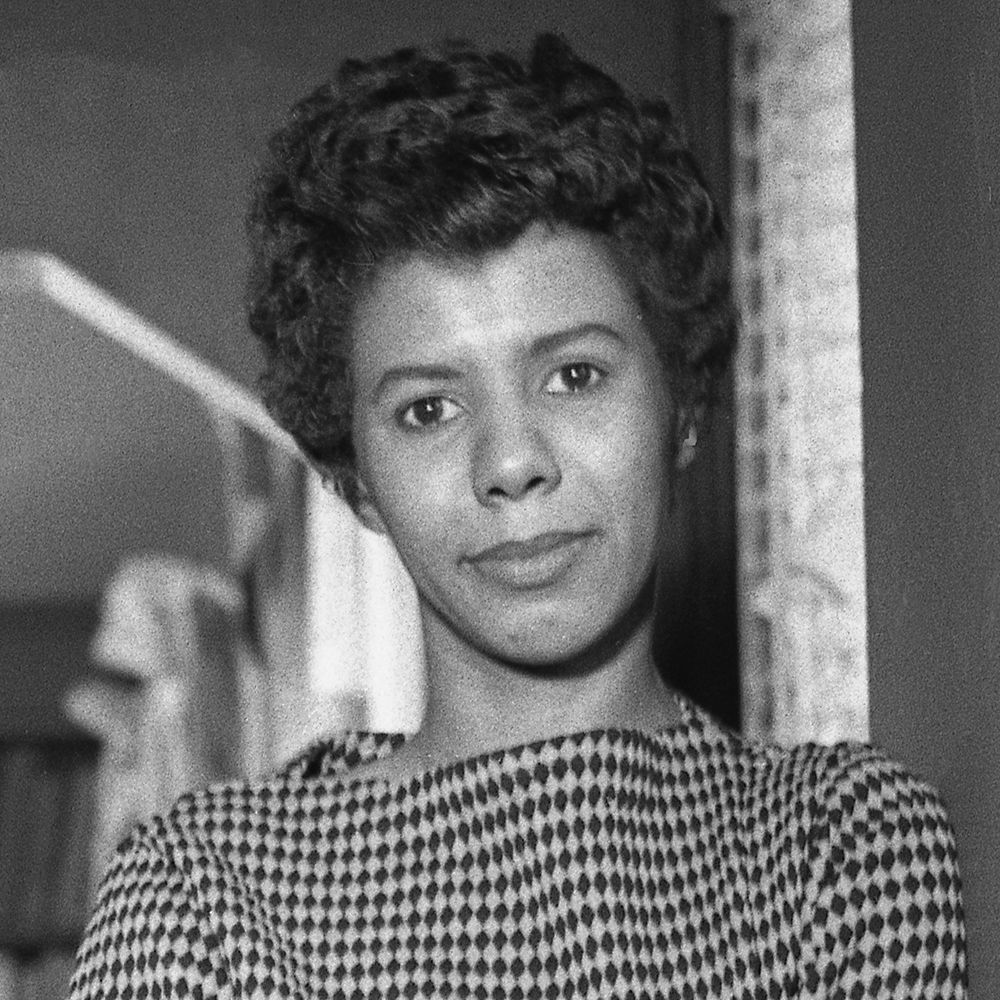 Close-up black-and-white image of Lorraine Hansberry, softly smiling with a confident gaze, dressed in a patterned blouse.
