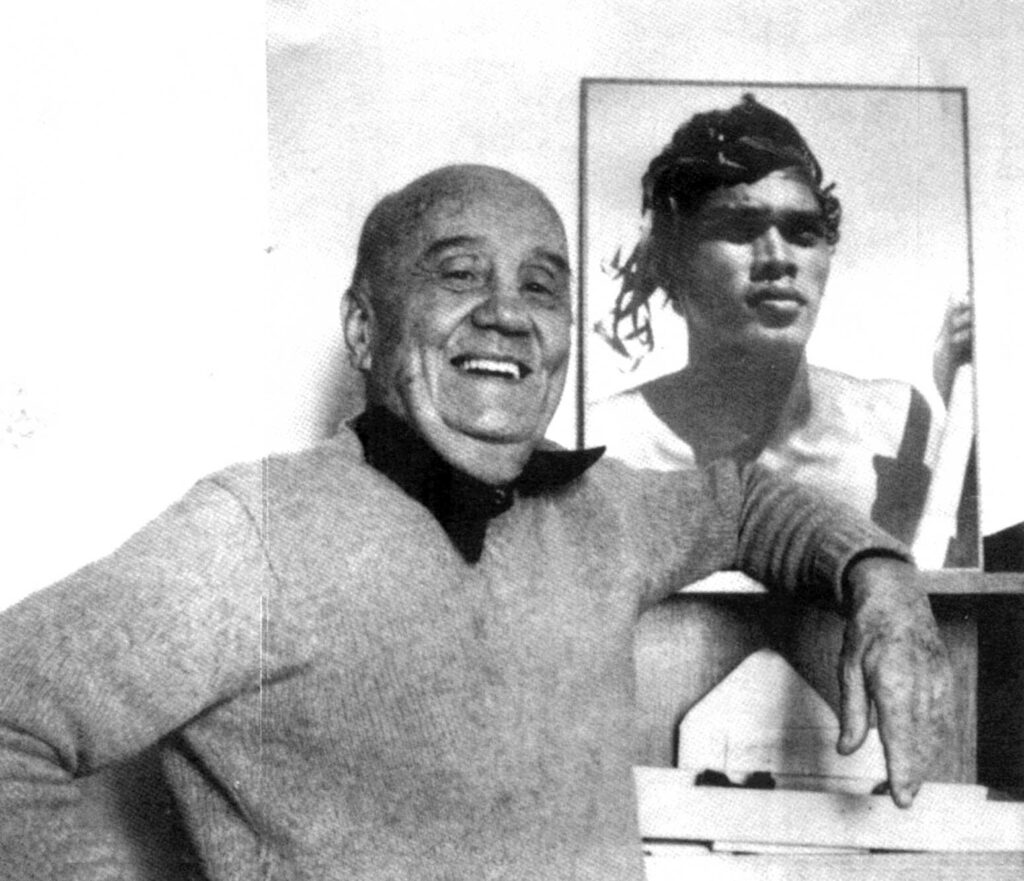 Similar to the previous image, Daniel Guérin is seen laughing with the same photograph of a young man behind him, cropped more closely.