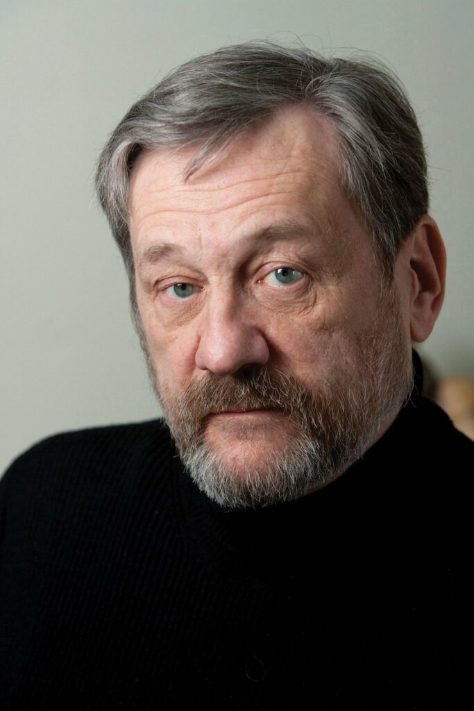 A recent headshot of Michael Bronski in a black turtleneck, with soft lighting on his face. He looks directly into the camera, conveying a thoughtful presence.